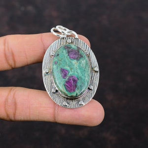Pode incluir: Pingente oval com uma gema verde e rosa engastada em uma moldura de prata. O pingente tem uma borda de prata texturizada com pequenos pontos de prata.