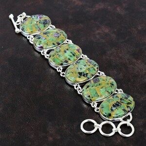May include: A silver bracelet with green, gold, and black oval-shaped stones. The bracelet has a lobster clasp closure.