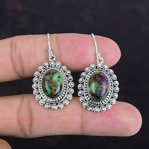 May include: A pair of silver earrings with green and purple gemstone oval cabochons set in a beaded bezel. The earrings have a simple hook closure.