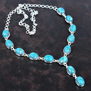 May include: A silver chain necklace with turquoise oval-shaped stones. The necklace has a drop pendant with a turquoise stone.