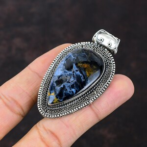 Pu&ograve; includere: Un ciondolo d'argento con una pietra di occhio di tigre blu e oro. Il ciondolo ha la forma di una lacrima ed &egrave; ornato da un bordo in argento dettagliato.
