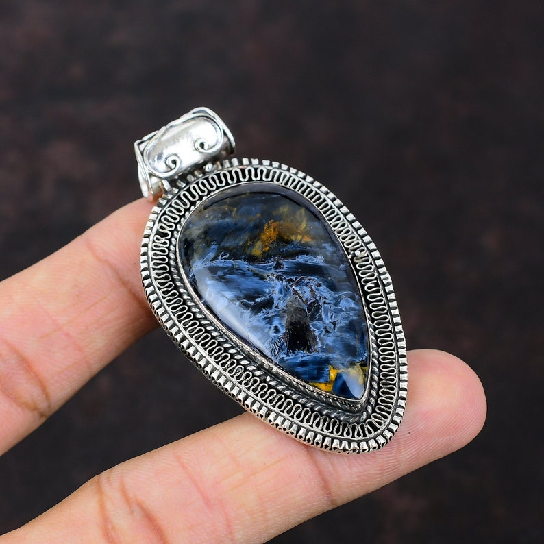 Pu&ograve; includere: Un ciondolo d'argento con una pietra di occhio di tigre blu e oro. Il ciondolo ha la forma di una lacrima ed &egrave; decorato con un bordo in argento dettagliato.