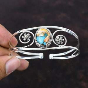 Könnte beinhalten: Silbernes Armreif-Armband mit einem geschwungenen Design und einem großen ovalen Türkis-Cabochon-Stein in der Mitte.