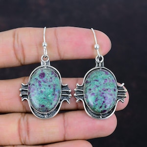 Peut inclure: Une paire de boucles d'oreilles en argent avec des accents de pierres précieuses ovales vertes et violettes. Les boucles d'oreilles ont un design détaillé avec un cadre en argent autour des pierres précieuses.