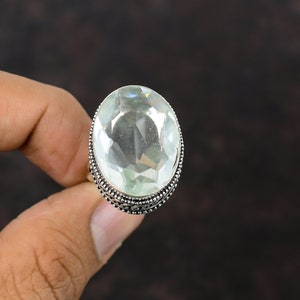 May include: A silver ring with a large, clear oval-shaped gemstone. The ring has a decorative, ornate band.