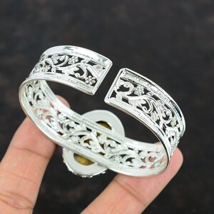 May include: Silver bangle bracelet with an intricate floral design and a large oval gemstone in the center.