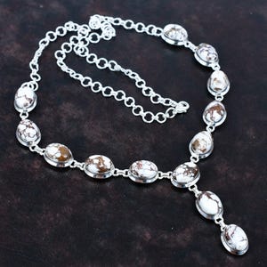 May include: A silver necklace featuring oval-shaped white and brown stones. The stones are set in a silver metal frame and connected by a delicate silver chain. The necklace has a Y-shaped pendant design.