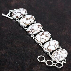 May include: A silver bracelet with a chain and seven oval-shaped white and brown stones. The stones have a marbled pattern.