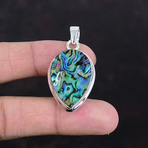 Op de afbeelding: Een druppelvormige hanger met een levendige abalone schelpinleg. De schelp toont iriserende blauwe, groene en paarse kleuren, gezet in een gepolijste zilveren lijst. De hanger is opgehangen aan een zilveren balein.