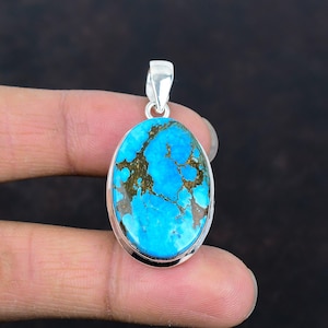 Pode incluir: Pingente oval de turquesa com uma argola de prata. O pingente apresenta uma pedra azul vibrante com padrões de matriz marrom. A pedra é definida em uma moldura de prata polida. Uma bela joia.