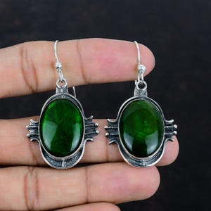 Puede incluir: Un par de pendientes colgantes con piedras cabujón ovaladas de color verde intenso engastadas en plata de ley oxidada. Los engastes de plata tienen un diseño decorativo de múltiples puntas en los laterales e incluyen ganchos de plata.