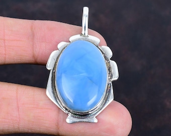 May include: A silver pendant featuring a large, oval, light blue gemstone. The gemstone is set in a decorative silver frame with a loop at the top for a chain. The pendant is held in a hand.