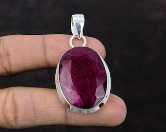 Può includere: Un ciondolo d'argento con una grande pietra di rubino di forma ovale. Il rubino è di colore rosso intenso e ha una taglio sfaccettato. Il ciondolo è incastonato in una montatura a castone d'argento.