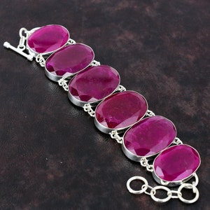 May include: A silver bracelet featuring six large, oval-cut, deep red gemstones. The gemstones are set in individual silver bezels and connected by small silver chain links. The bracelet has a toggle clasp.