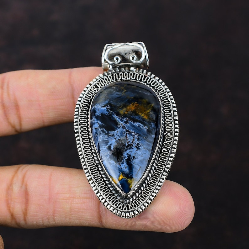 Pu&ograve; includere: Un ciondolo d'argento con una pietra di occhio di tigre blu e oro. Il ciondolo ha la forma di una lacrima e ha un bordo d'argento intricato.
