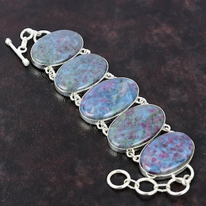 May include: A silver bracelet with six oval-shaped blue and pink gemstones. The bracelet has a toggle clasp.