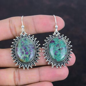 May include: A pair of silver earrings with green and pink oval stones set in a sunburst design.