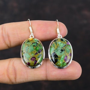 May include: Oval-shaped earrings with a silver frame. The earrings feature a mosaic of green, gold, and red stones. The earrings are suspended from a silver hook.