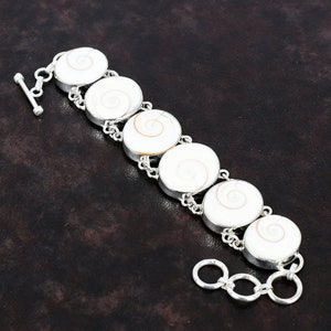 May include: A silver bracelet with a toggle clasp features seven round white shell charms with a spiral pattern.