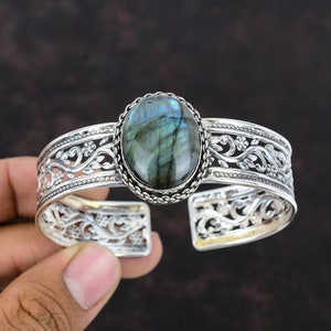 May include: Silver cuff bracelet featuring a large oval labradorite gemstone set in a silver filigree design.