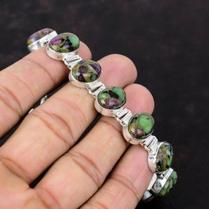 May include: A silver bracelet featuring green and pink gemstones. The bracelet has a chain link design and is made from sterling silver.