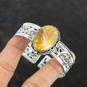 May include: A silver cuff bracelet with an oval-shaped yellow and brown jasper stone set in the center. The bracelet has a delicate floral design.