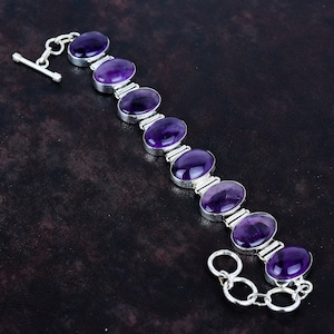 Puede incluir: Una pulsera de plata con piedras de amatista ovaladas de color púrpura intenso. Las piedras preciosas están engastadas en biseles individuales de plata y conectadas por eslabones de plata. La pulsera tiene un cierre de palanca.