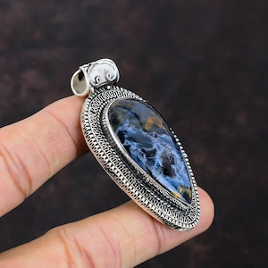 Pu&ograve; includere: Ciondolo in argento con una pietra di occhio di tigre blu e oro incastonata in una cornice d'argento dettagliata.