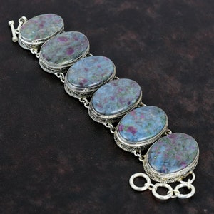 May include: A silver bracelet with six oval-shaped blue and pink gemstones. The bracelet has a delicate filigree design and a clasp.
