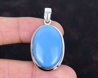 May include: Oval-shaped pendant with a light blue gemstone set in a silver-colored metal frame. The pendant has a smooth, polished surface and a loop at the top for a chain. The gemstone is approximately 1.5 inches long.