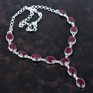 May include: A silver necklace featuring oval-cut, deep red gemstones. The gemstones are set in individual bezels and connected by a delicate silver chain. The necklace has a Y-shaped pendant with three gemstones.