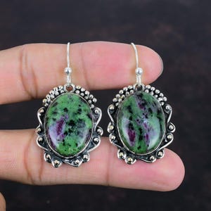 Può includere: Un paio di orecchini d'argento con pietre ovali verdi e rosa incastonate in montature d'argento ornate.