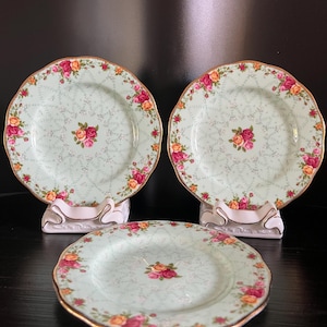 May include: Three vintage floral patterned dessert plates with a gold rim. The plates are light green with a floral pattern in shades of pink, yellow, and red.
