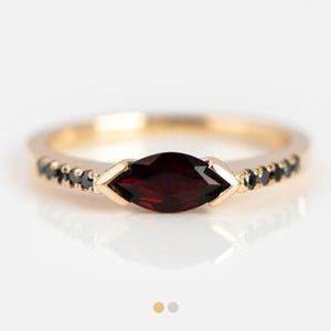 Könnte beinhalten: Ein goldener Ring mit einem roten Marquise-Schliff-Stein und schwarzen Diamanten, die in Pavé-Fassung gefasst sind.