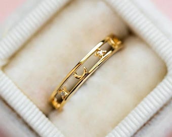 May include: A gold ring with a delicate design featuring crescent moons and small sparkling stones. The ring is displayed in a white ring box.