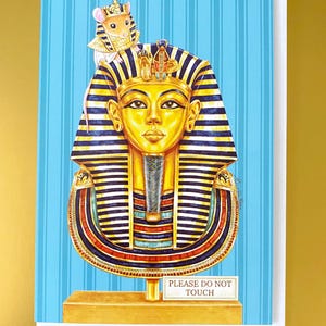 May include: Greeting card depicting a golden pharaoh's mask with a mouse wearing a pharaoh's headdress. The background is light blue with vertical stripes. The card has the text "PLEASE DO NOT TOUCH" on a small sign.