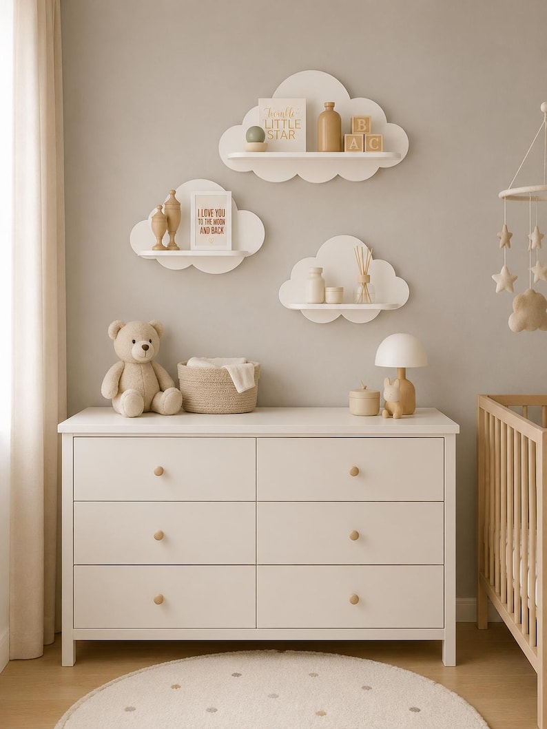 Peut inclure: Trois &eacute;tag&egrave;res murales blanches en forme de nuage portant de petits objets d&eacute;coratifs, dont un panneau indiquant Twinkle Little Star et un autre I Love You To The Moon And Back, au-dessus d'une commode blanche &agrave; six tiroirs avec des boutons en bois.
