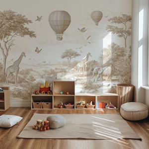Op de afbeelding: Een kinderkamer met een safari-thema muurschildering met giraffen, zebra's en een olifant. Houten speelgoedopbergkubussen zijn voor de muurschildering geplaatst, met speelgoed en manden erin. Een beige tapijt en een ronde poef maken de kamerdecoratie compleet.