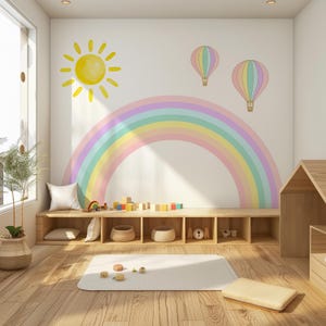 Puede incluir: Un conjunto de vinilos decorativos con un gran arcoíris en tonos pastel, un sol amarillo brillante y dos globos aerostáticos en colores suaves. El diseño está aplicado sobre una pared blanca encima de un mueble de madera con compartimentos.