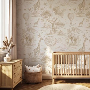 Op de afbeelding: Een kinderkamer met beige en wit behang met een safarithema met giraffen, olifanten, luchtballonnen en vogels. De kamer heeft een houten wieg, een dressoir en een gevlochten mand met kussens.
