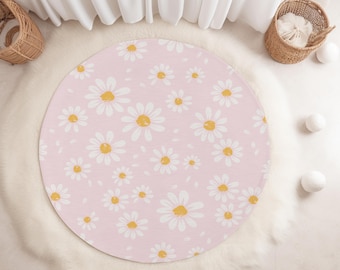 May include: A round, pink rug with a daisy pattern. The rug features white daisies with yellow centers scattered across the surface. The rug is surrounded by a white, fluffy material. Two wicker baskets and white spheres are also visible.
