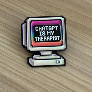 May include: A pixel art style pin shaped like a vintage computer monitor. The screen displays a rainbow gradient background with the white text CHATGPT IS MY THERAPIST. The monitor casing is light grey with black outlines and a small square button.