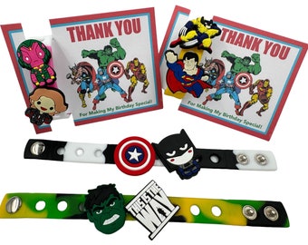 May include: Two colorful silicone bracelets with superhero character charms. The bracelets are black and white, and green, yellow, and black. The charms include Captain America, Hulk, Batman, Superman, Wolverine, and Black Widow. The bracelets have the text "This is the way" on one of them. The image also includes two thank you cards with superhero characters.