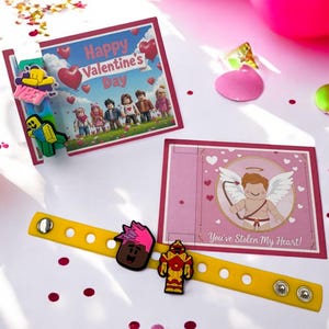 Könnte beinhalten: Valentinstagskarten und ein gelbes Armband mit Charakteranhängern. Eine Karte zeigt "Happy Valentine's Day" mit Cartoonfiguren. Die andere Karte zeigt Amor und den Text "You've Stolen My Heart!"