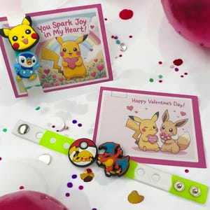 Könnte beinhalten: Artikel zum Valentinstag mit Pikachu und anderen Pokémon-Charakteren. Enthält ein grün-weißes Armband mit Anhängern und Karten mit dem Text "You Spark Joy in My Heart!" und "Happy Valentine's Day!"