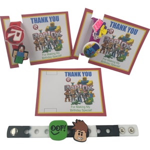 May include: Three thank you cards with a Roblox theme. Each card has a red border and the text "Thank You" in blue. The cards feature a Roblox logo and the text "For Making My Birthday Special!"  The cards are accompanied by a black and white wristband with a Roblox character and the text "OOF!" in green.