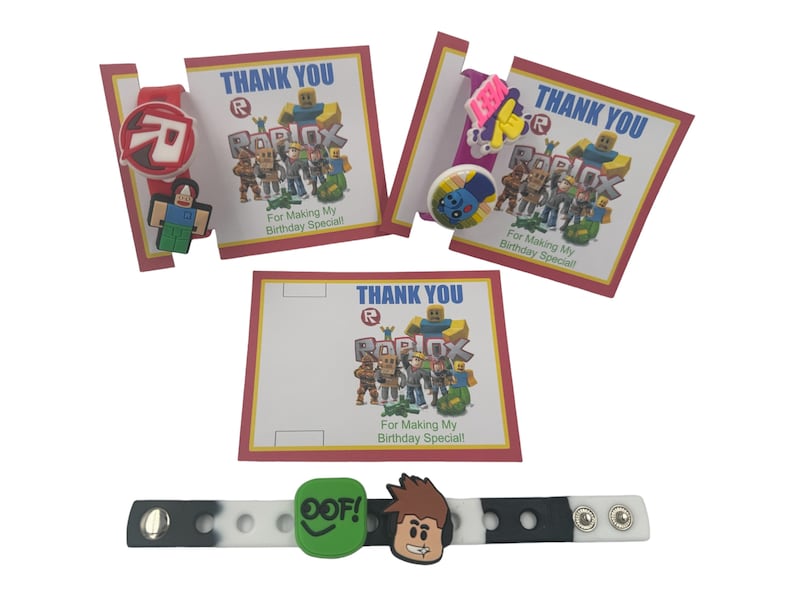 May include: Three thank you cards with a Roblox theme. Each card has a red border and the text "Thank You" in blue. The cards feature a Roblox logo and the text "For Making My Birthday Special!"  The cards are accompanied by a black and white wristband with a Roblox character and the text "OOF!" in green.