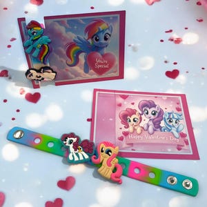 Könnte beinhalten: Ein farbenfrohes Armband mit My Little Pony-Anhängern und Valentinstagskarten. Das Armband hat einen Farbverlauf von Blau, Grün, Rosa und Gelb. Die Karten zeigen Cartoon-Ponys und den Text "You're Special" und "Happy Valentine's Day".