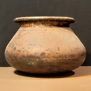 May include: A brown clay pot with a rounded body and a wide opening. The pot has a rustic, aged appearance.
