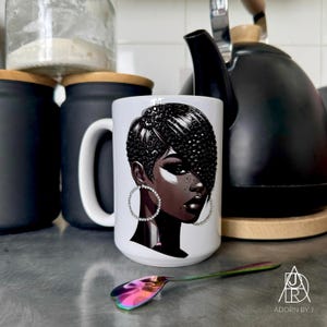 Peut inclure: Mug en céramique blanche avec une illustration détaillée d'une femme noire avec une coiffure élégante et des créoles. Une cuillère colorée repose devant le mug. Des bocaux noirs et une bouilloire noire sont en arrière-plan.